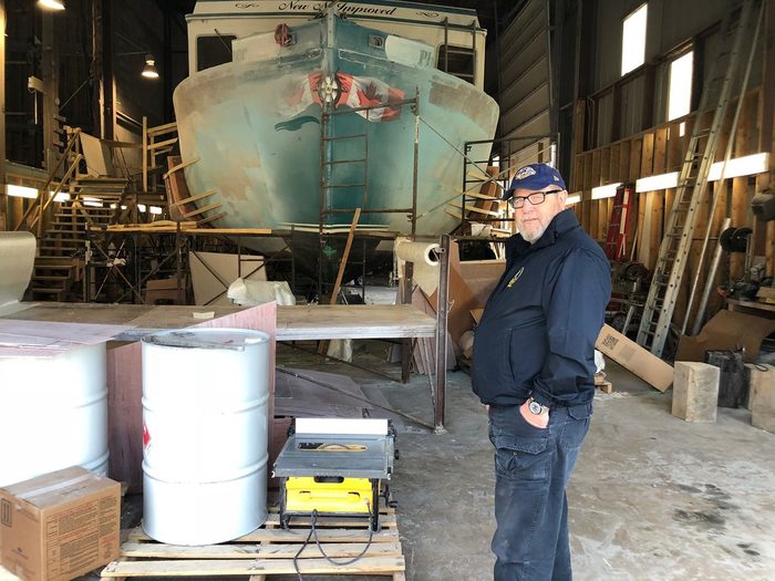 A man standing in front of a fishing vessel in dry dock.
