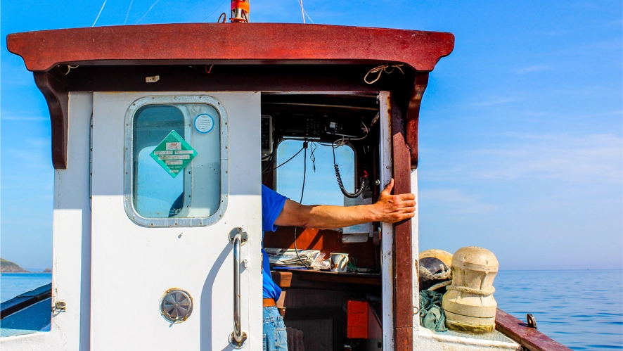 A person standing in the helm of a fishing vessel.